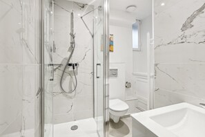 A modern bathroom with a glass-enclosed shower, a white toilet, and a sink. - Charmant Appt Avec Balcon - Ternes- Bail Mobilit (Paris)