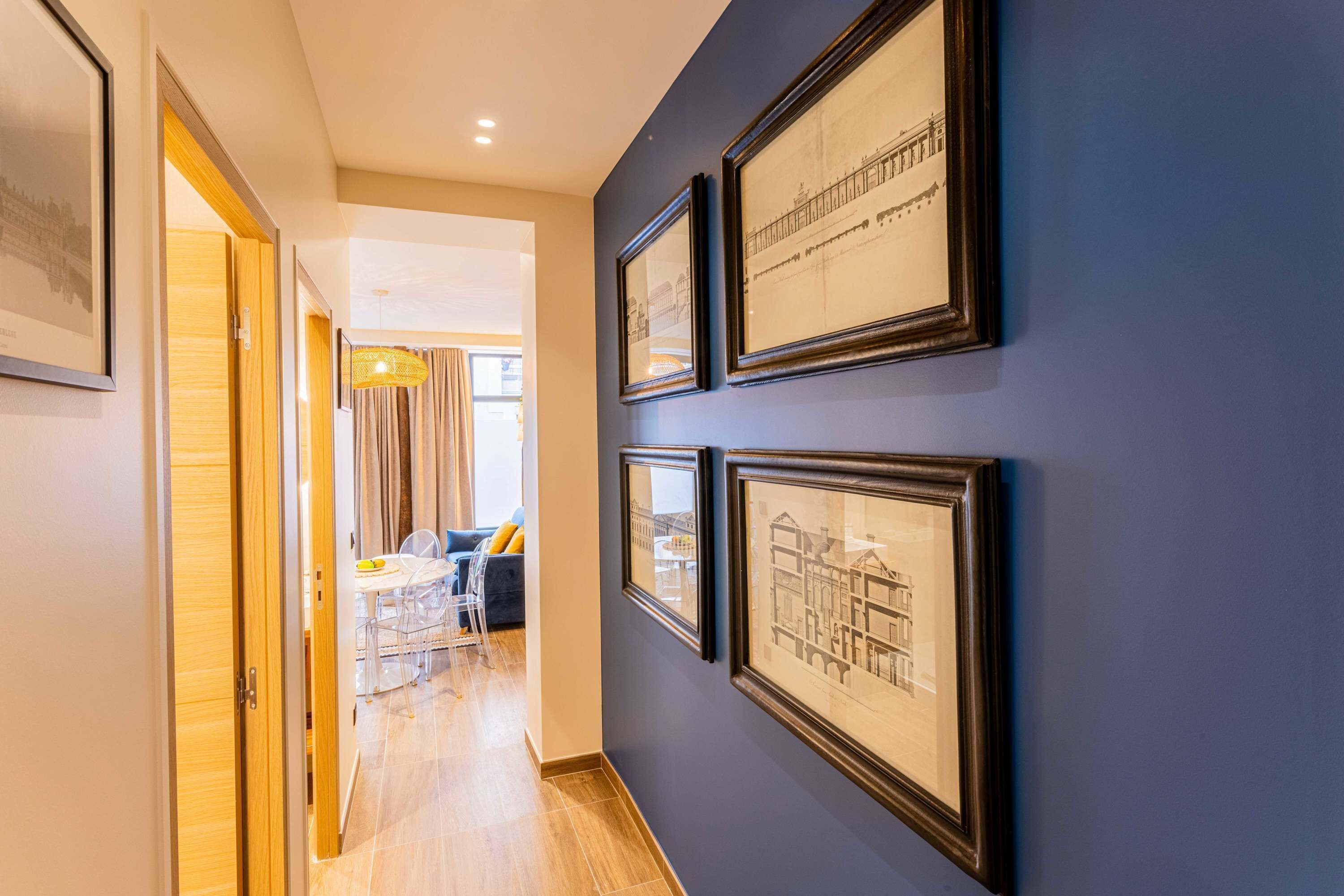 A hallway with framed architectural drawings on the wall, leading to a dining area with a table and chairs.