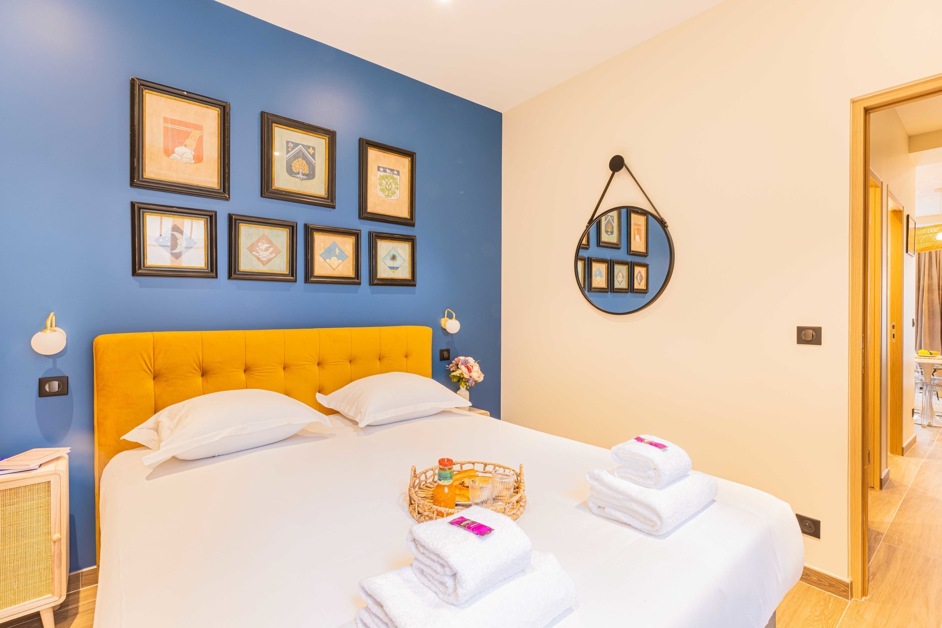Een hotelkamer met een groot bed, hoofdeinde, een spiegel aan de muur en ingekaderde foto's.