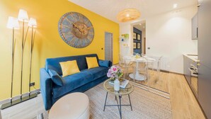 A modern living room with a blue sofa, a large wall clock, and a dining area with a round table and chairs. - Amazing Apartment - 2BR 6P - Gare du Nord (Paris)