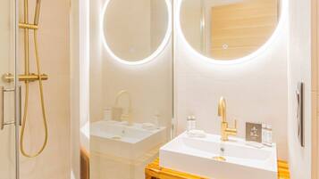 A modern bathroom with a glass-enclosed shower, a white sink with a gold faucet, and wooden vanity.