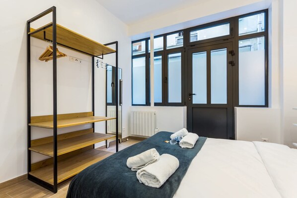 A bedroom with a bed, a wooden shelf unit, and a large window with a view of buildings. - Amazing Apartment - 2br6p - Bastille (Paris)
