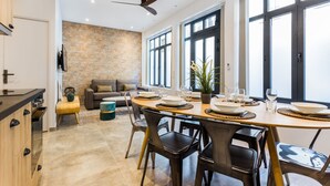 A modern kitchen with a dining area, featuring a brick wall, large windows, and a ceiling fan. - Amazing Apartment - 2br6p - Bastille (Paris)