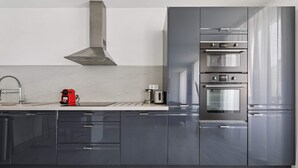 A modern kitchen with dark cabinets, stainless steel appliances, and a red coffee maker. - Charmant Appt 1brd 2P - Neuilly-sur-seine (Neuilly-sur-Seine)