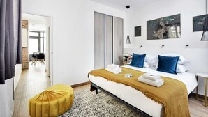 Een moderne slaapkamer met een groot bed, een geel poefje en een kamerkleed met een patroon.