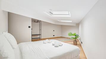 A modern bedroom with a large bed, skylights, a small plant, and a wooden floor.
