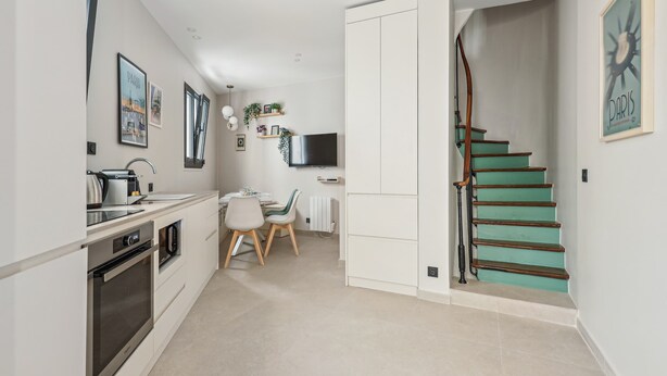 A modern kitchen with a dining area, a staircase, and a TV mounted on the wall. - Maison Atypique de 82 m (Vincennes)