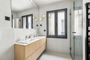 A modern bathroom with two sinks, wooden cabinets, a large mirror, and a glass shower enclosure. - Maison Atypique de 82 m (Vincennes)