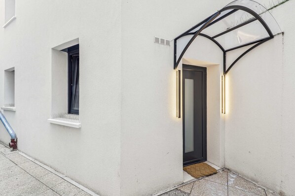 A white building with a small window and a door with a glass entryway. - Maison Atypique de 82 m (Vincennes)