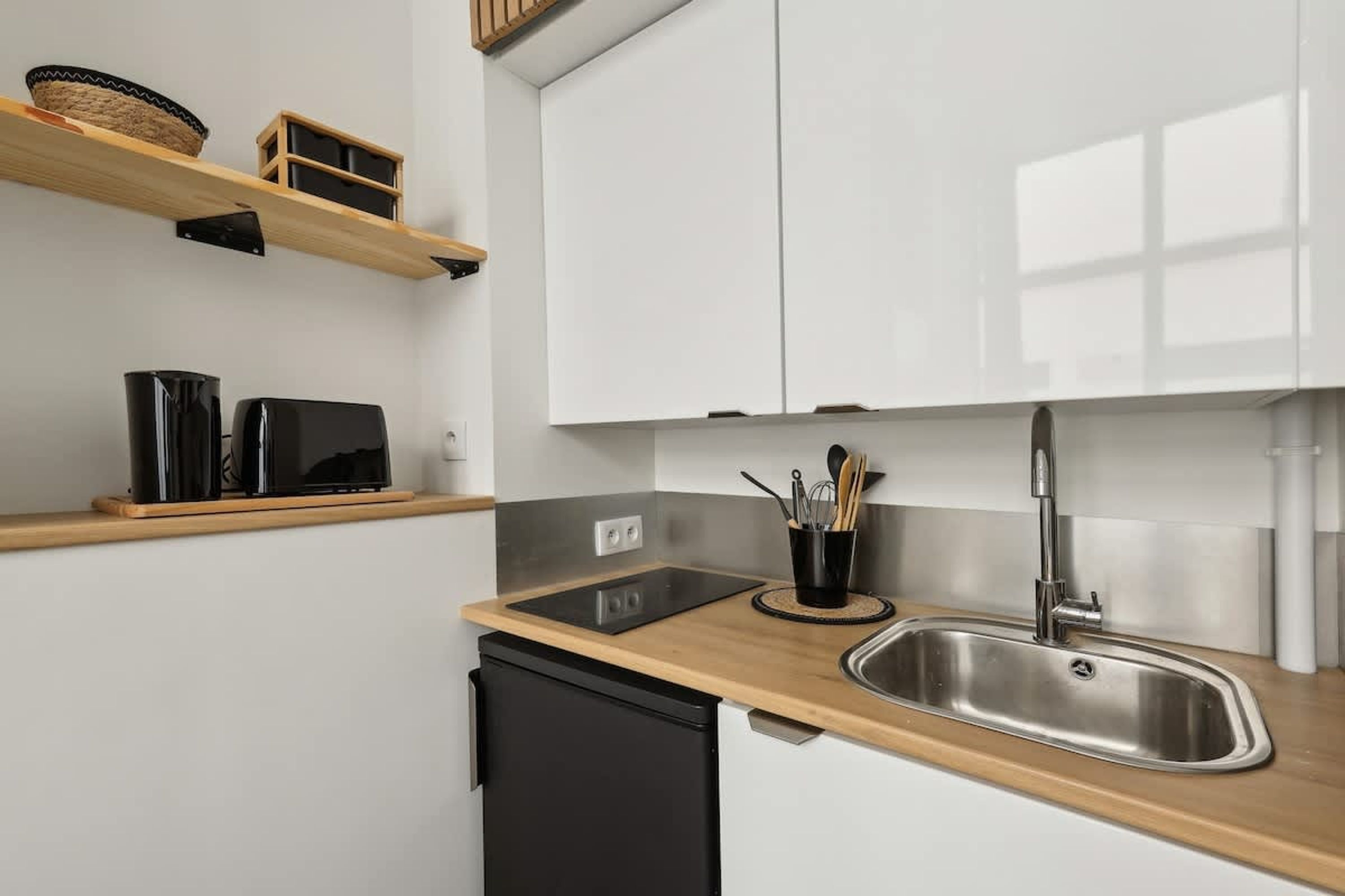 Una cocina moderna con encimera de madera, pileta de acero inoxidable y lavavajillas negro. Hay estantes de madera sobre la encimera con cestas y recipientes.