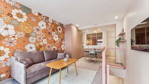 A modern living room with a floral wallpaper, a sofa, a coffee table, and a dining area with a glass railing. - Elegant Apartment - 2 Bedroom -6people (Paris)