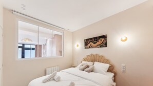 A bedroom with a large mirror, a bed with white linens, a headboard with a scalloped design, and a painting on the wall. - Elegant Apartment - 2 Bedroom -6people (Paris)