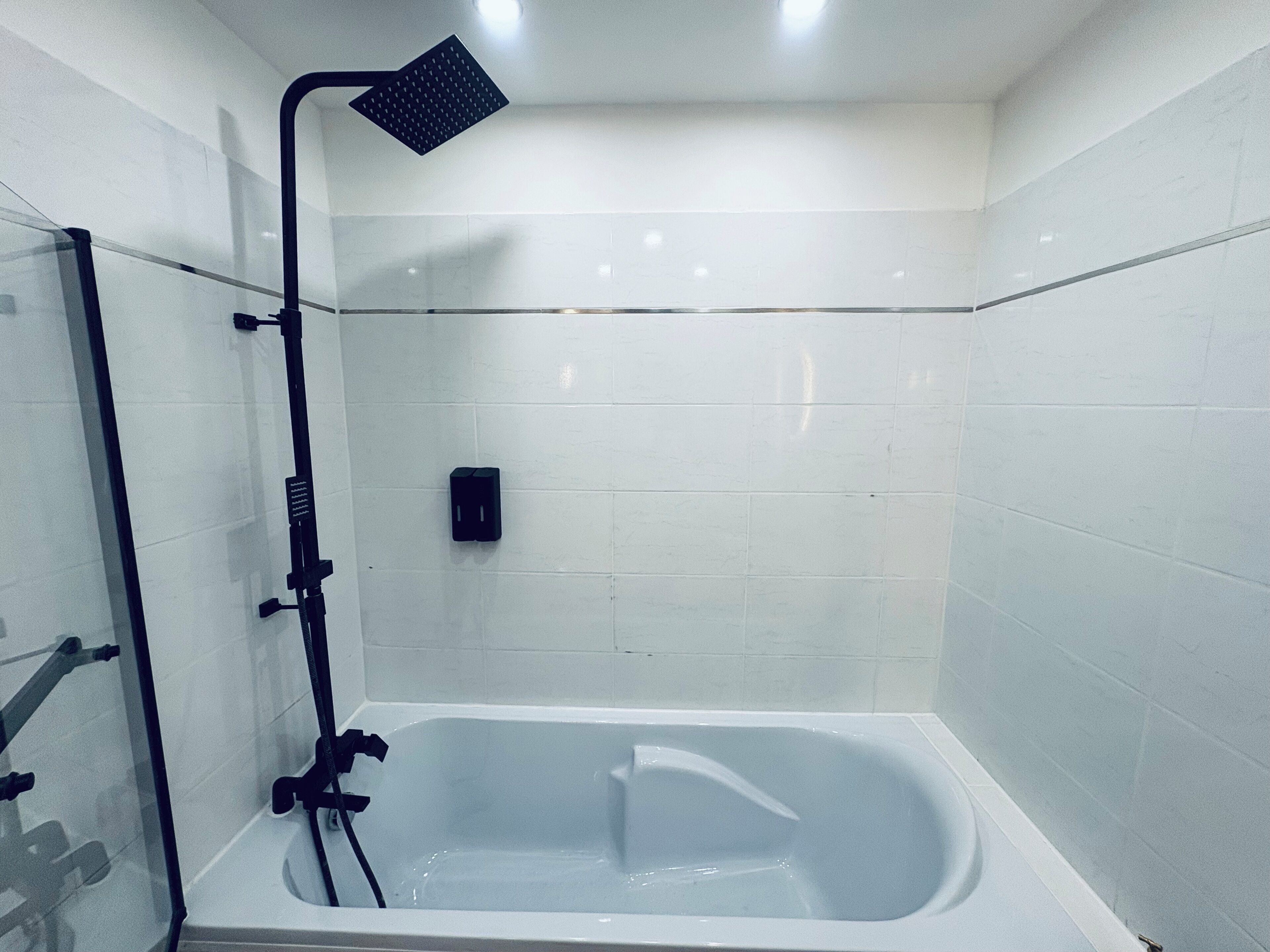 A bathroom with a bathtub, a showerhead, and a hand dryer.