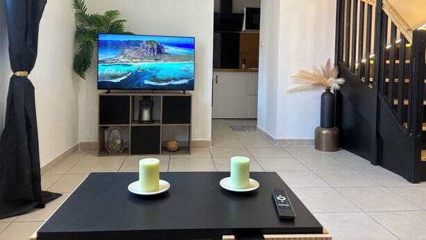 A living room with a flat-screen TV on a stand, two candles on a table, a remote control, and a staircase with a railing. - Superb 6-person 80m2 apartment in Agde (Agde)