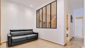 Una sala moderna con un sofá gris, un espejo grande y piso de madera.