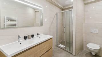 A modern bathroom with a large mirror, a white sink, a glass shower enclosure, and a toilet.
