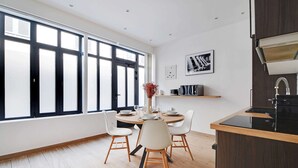 A modern dining area with a round table, white chairs, and a large window with blinds. - Amazing Apartment - 2BR 6P - Bastille (Paris)