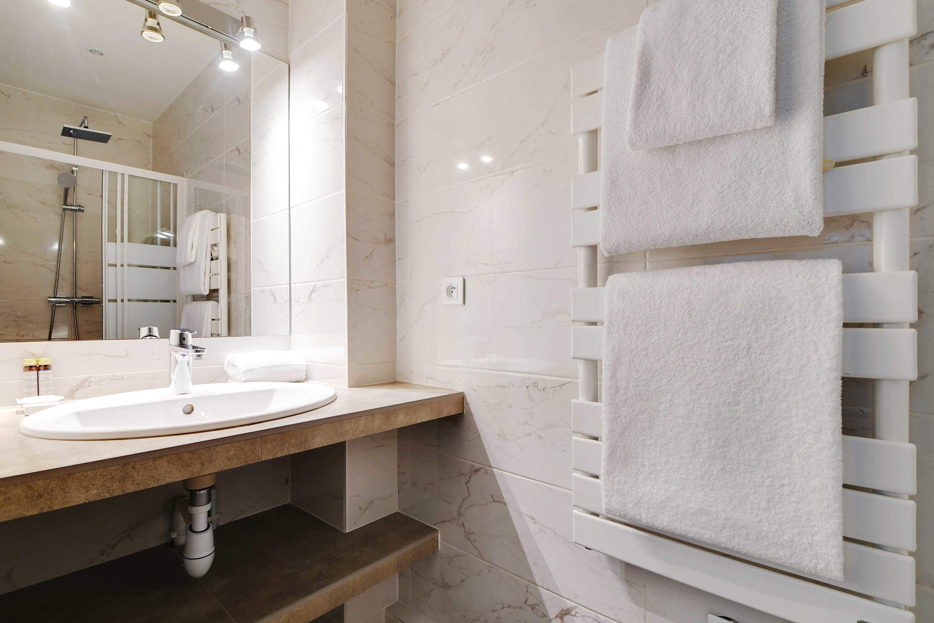 Un baño moderno con un lavamanos de mármol, cabina de ducha de vidrio y un perchero con varias toallas.