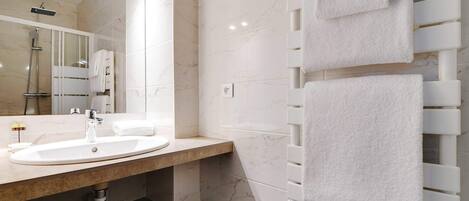 Un baño moderno con un lavamanos de mármol, cabina de ducha de vidrio y un perchero con varias toallas.
