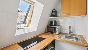 Una cocina compacta con estufa integrada, microondas, lavabo y ventana con vistas a un paisaje urbano.