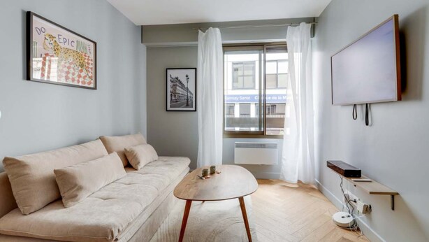 Un salon moderne avec un canapé beige, une table basse ronde en bois et un téléviseur à écran plat fixé au mur.