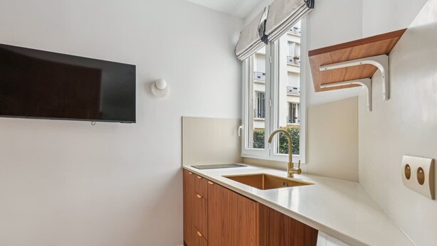 Une cuisine moderne avec des meubles en bois, un évier en acier inoxydable et une fenêtre donnant sur des immeubles.