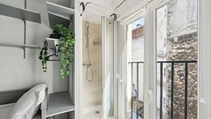 A bathroom with a shower, a window with a view of a building, and shelves with plants. - Cozy Studio - Rue Saint Maur - Mobility Lease (Paris)