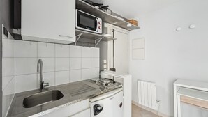 A compact kitchen with a built-in microwave, a sink, and a compact stove. - Cozy Studio - Rue Saint Maur - Mobility Lease (Paris)