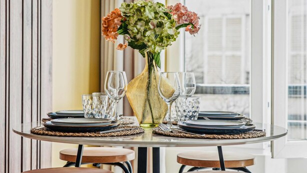 A dining table set with plates, cutlery, and glasses, centered with a vase of flowers. - Appartement Central 2bdr - 6P le Marais (Paris)