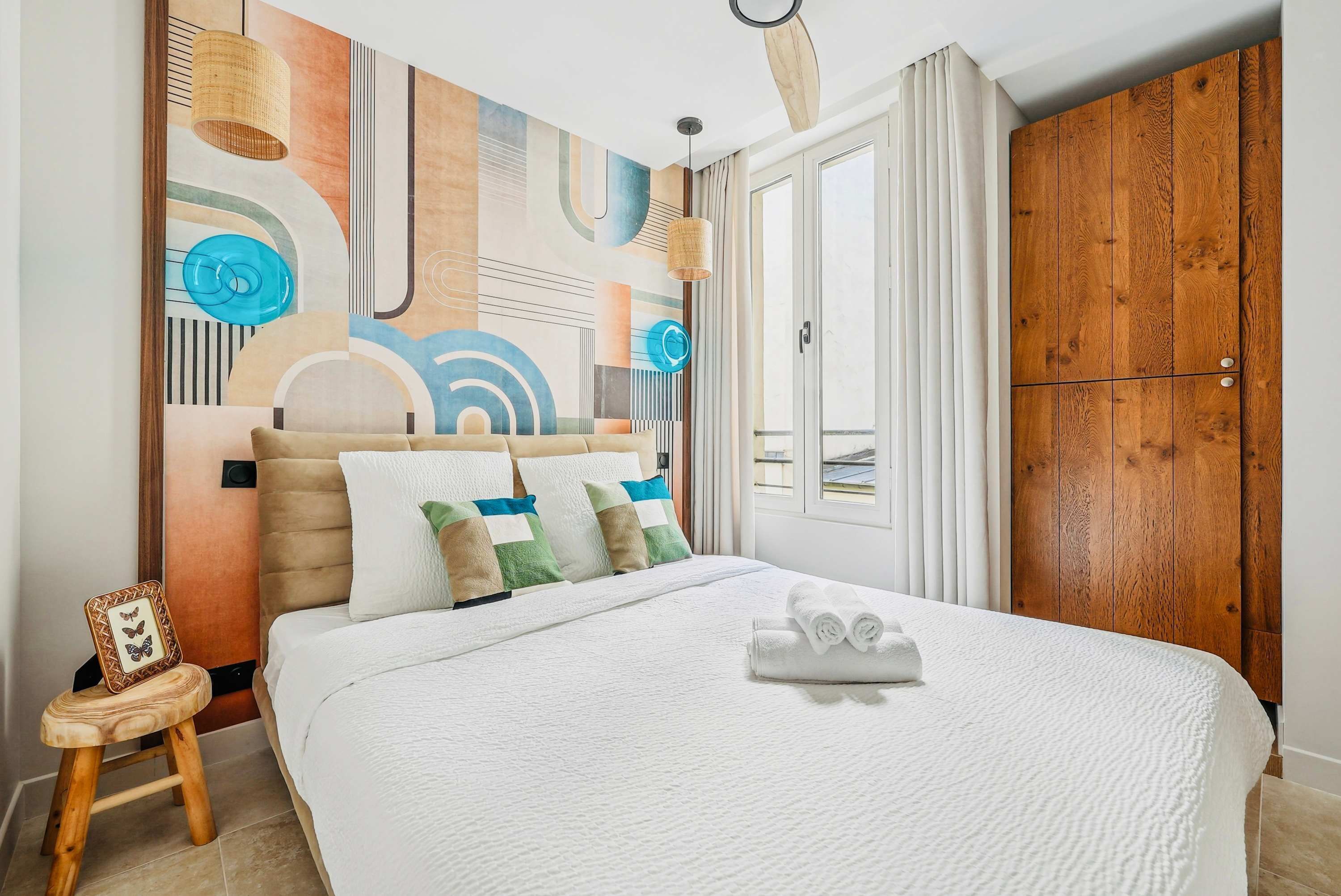 A hotel room with a large bed, a wooden wardrobe, and a wall with abstract art.