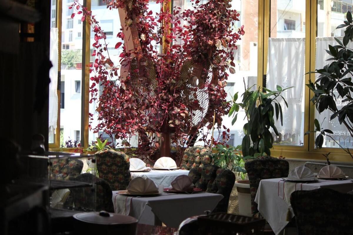 A restaurant with tables set for dining, surrounded by potted plants and a large tree with red leaves.