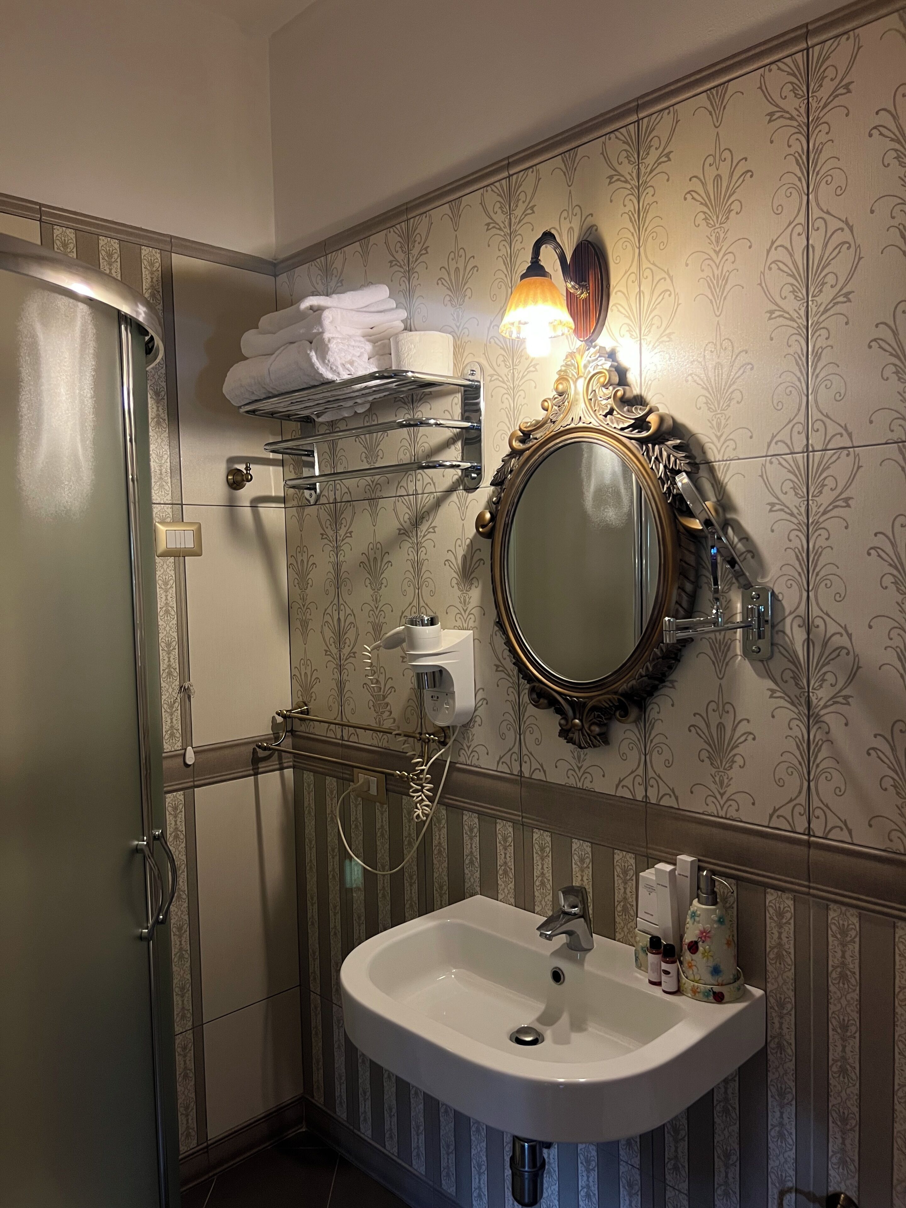 A bathroom with a shower, a sink with toiletries, a towel rack, and a mirror with a decorative frame.
