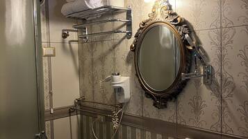 A bathroom with a shower, a sink with toiletries, a towel rack, and a mirror with a decorative frame.