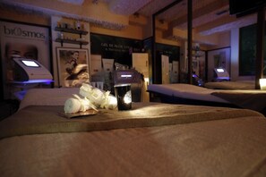 Una stanza spa con due lettini per massaggi, una bottiglia di lozione e una candela.