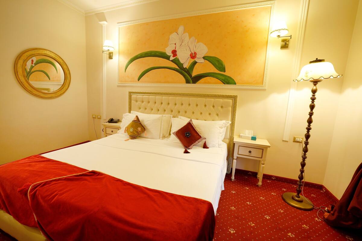 Ein Hotelzimmer mit einem großen Bett, einem Nachttisch, einer Lampe und einem Bild an der Wand.