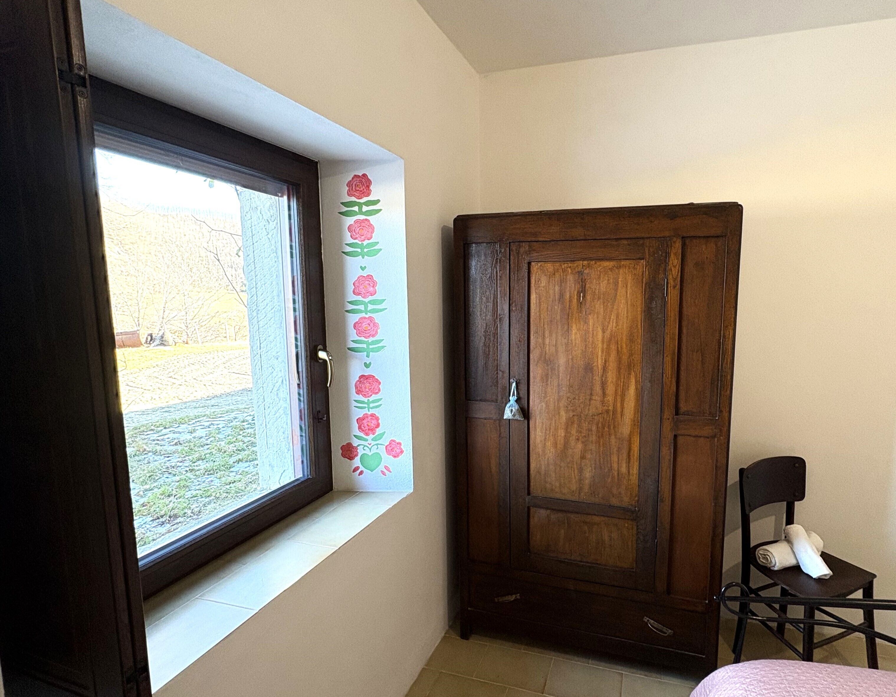 Een kamer met een groot raam, een houten garderobe, een stoel en een handdoek op de stoel.