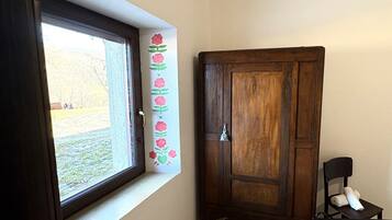 Een kamer met een groot raam, een houten garderobe, een stoel en een handdoek op de stoel.