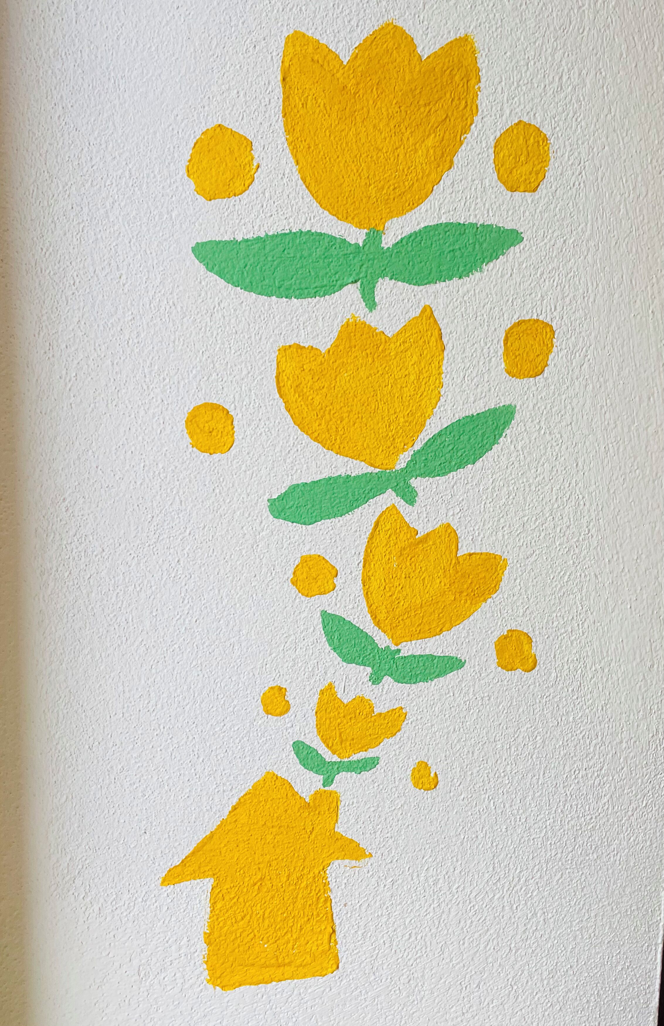 Un mur blanc à texture, orné d’un tableau abstrait aux couleurs jaune et verte représentant des fleurs et des feuilles.