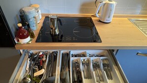 A kitchen counter with a coffee maker, kettle, and jar. Below, a drawer contains various utensils.