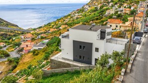 Un edificio moderno a due piani con tetto piatto, immerso in un quartiere collinare con case a terrazza.