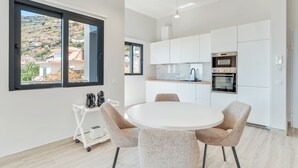 Una cucina moderna con mobili bianchi, un tavolo rotondo con sedie e vista su una collina attraverso ampie finestre.