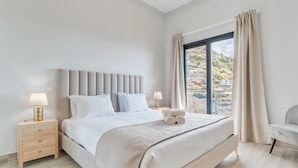 Una camera da letto moderna con un grande letto, lampade sui comodini, un tavolo da notte e vista su una collina attraverso una finestra.