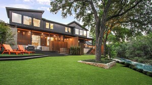 A modern two-story house with a well-maintained lawn, outdoor seating, and a small stream. - ATX South Lamar Creekside with Hot tub (Austin)