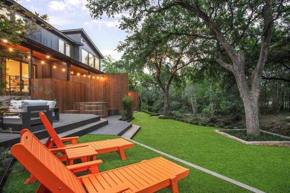 A modern house with a deck, outdoor seating, and a well-maintained lawn.