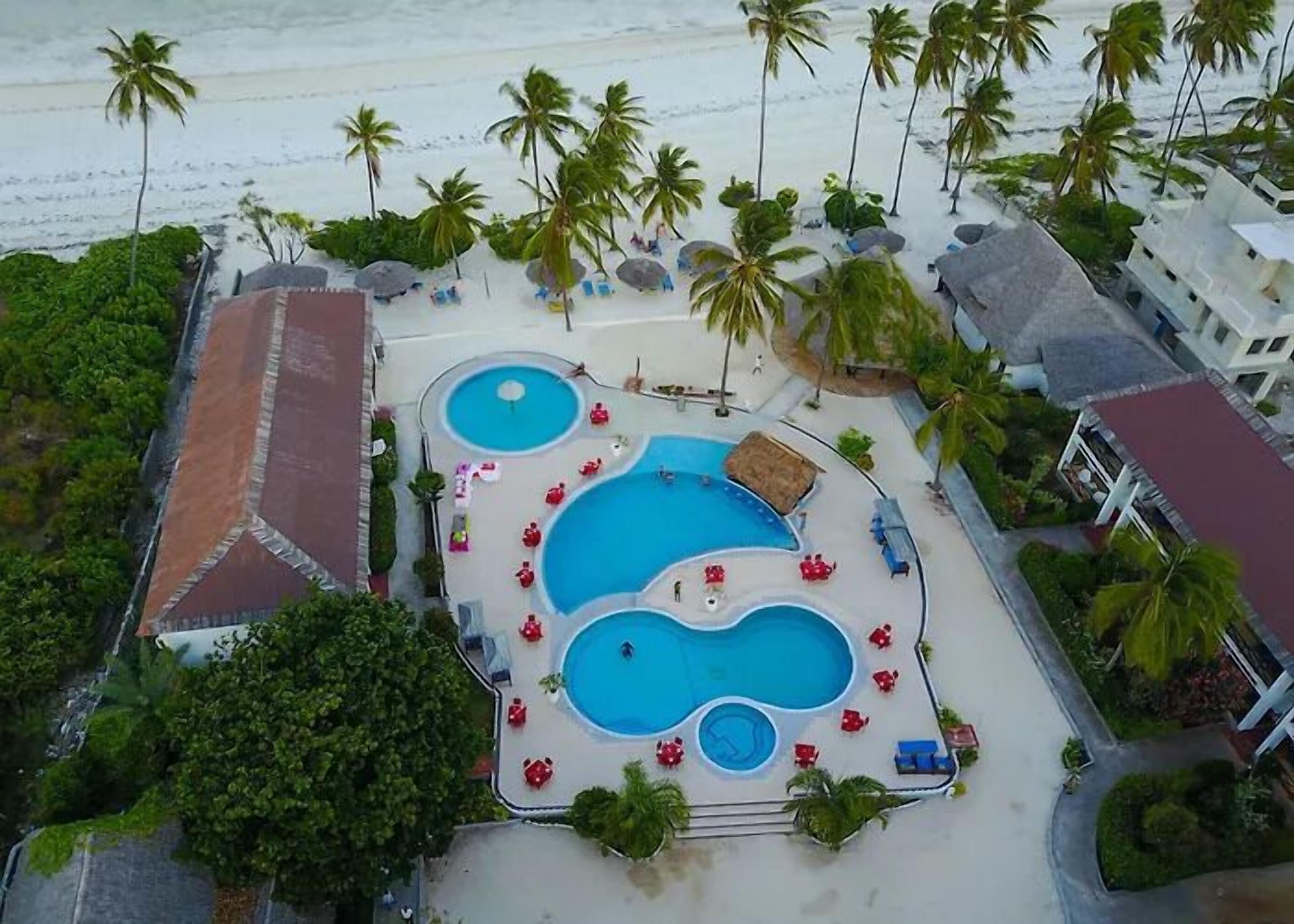 Vista aérea de um resort com várias piscinas, palmeiras e acesso à praia.