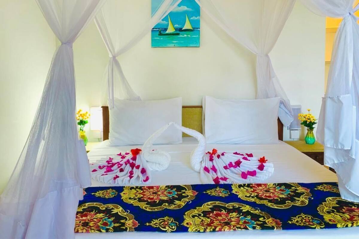 Una cama con dosel, almohadas blancas y una colcha estampada con motivos florales.
