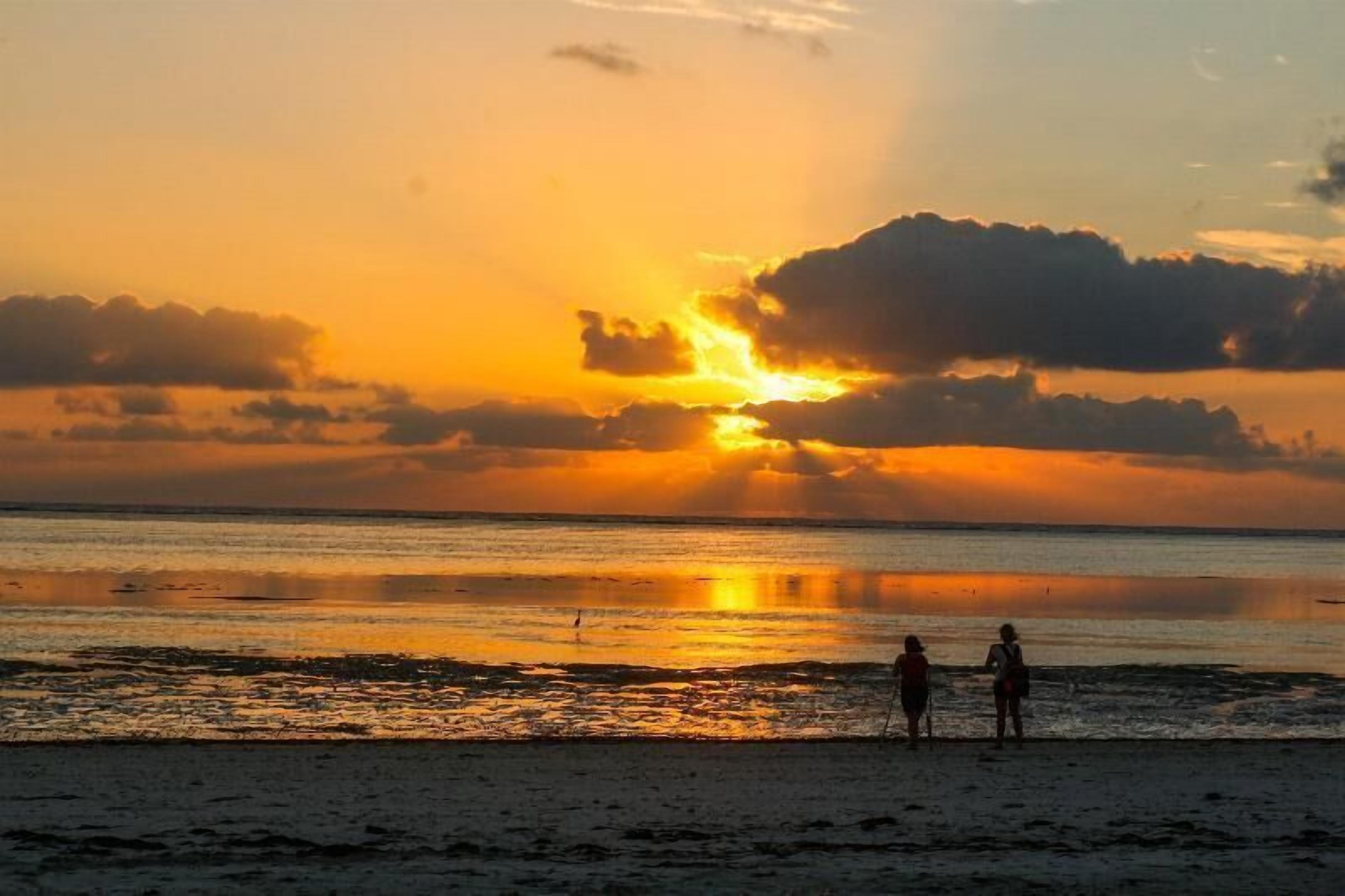 Un atardecer sobre una playa con dos personas de pie en la orilla.