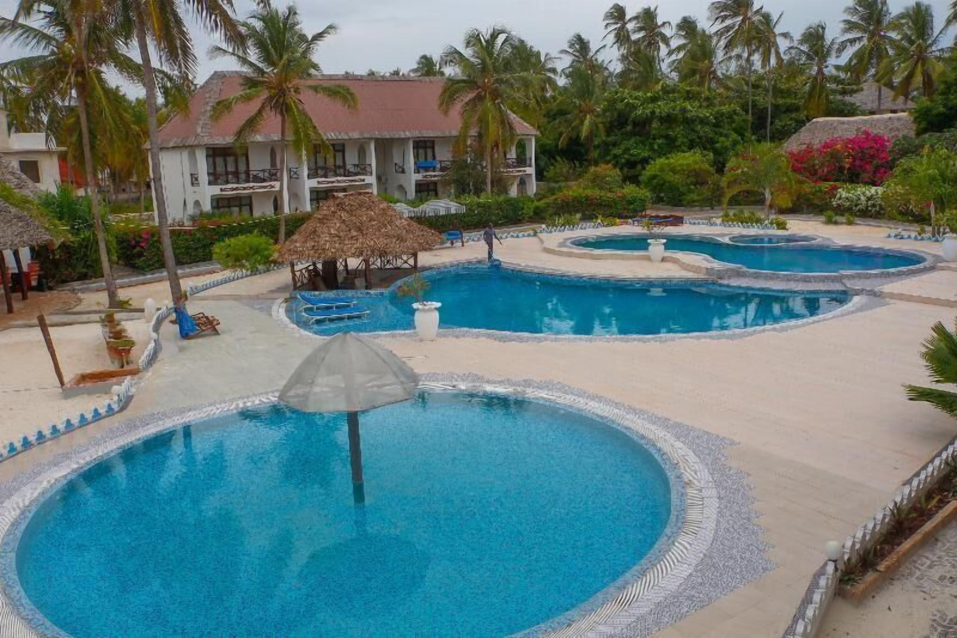 A resort with multiple swimming pools, palm trees, and a building with balconies.
