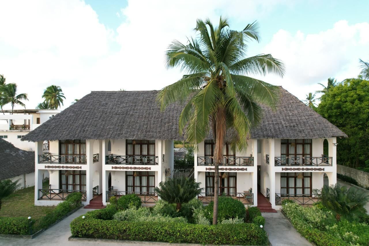 A two-story building with a thatched roof, surrounded by lush greenery and palm trees.