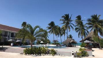 A beach resort with a pool, palm trees, and a building with a thatched roof.